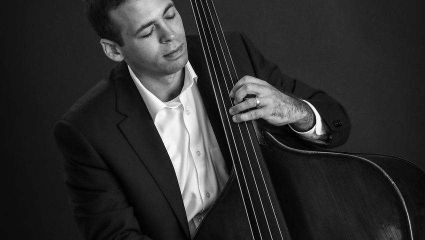 Black and white image of Eli Uttal Veroff seated playing stand up bass in dark blazer and white shirt