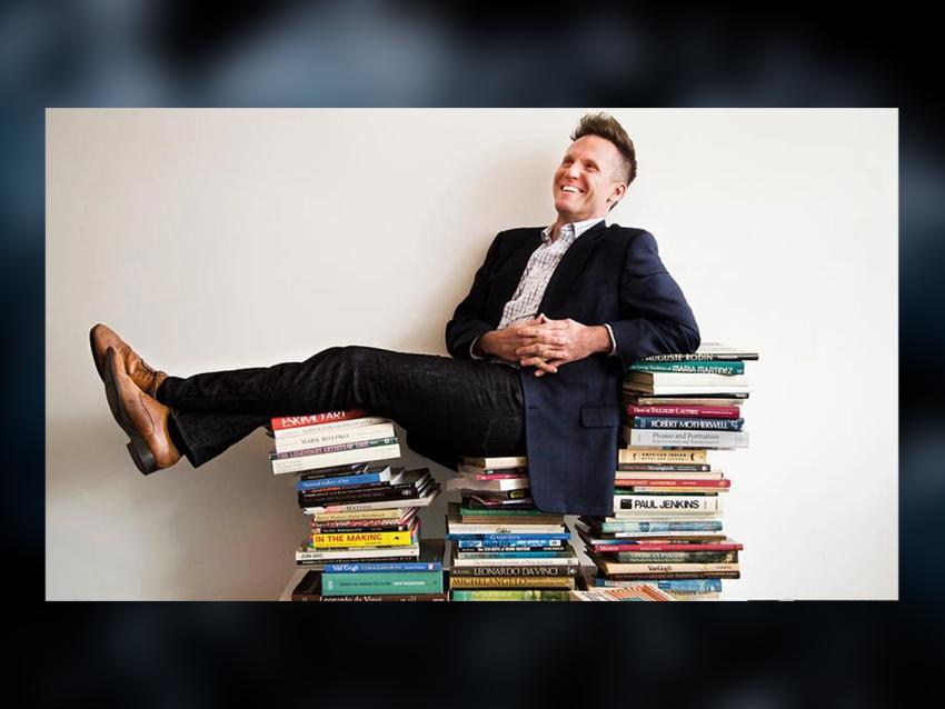 Image of Theo Edmonds wearing a dark suit sitting on a stack of books
