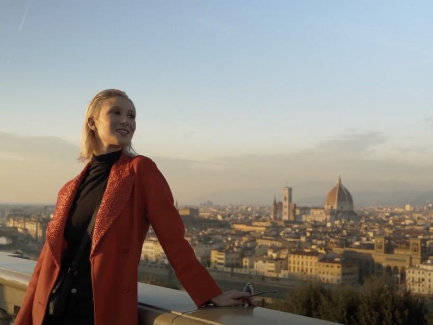 Film still of "Va Bene Così" a comedy short film written and directed by Peter Allen Stone that was filmed in Florence, Italy, woman in red coat stands on a bridge over looking Florence.