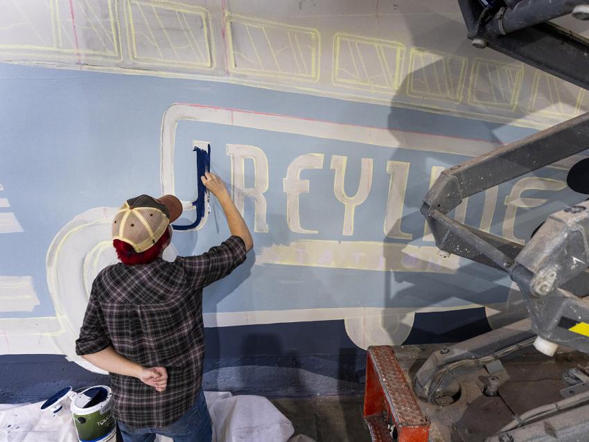 student painting word greyline on greyline station mural