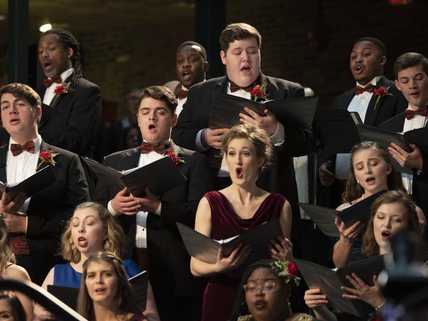 Singers wearing formal attire hold music binders while performing