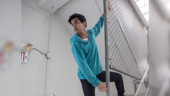 Image of Taha Mandviwala in a teal hoodie climbing a chain link fence