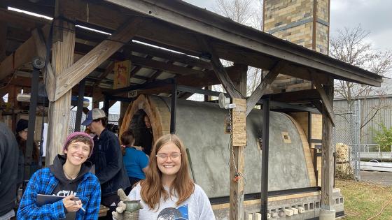 Students hold up finished ceramic pieces outside of new kiln