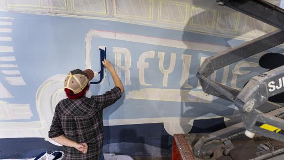 student painting word greyline on greyline station mural