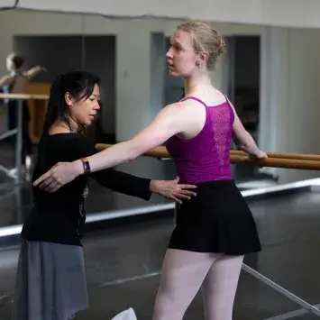 dancer at barre with instructor giving feedback
