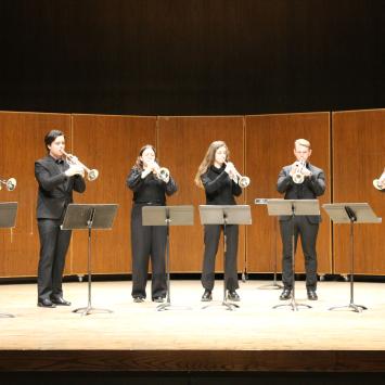Members of the Baroque Trumpet ensemble standing onstage wearing black clothing playing their instruments behind music stands