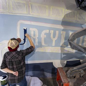 student painting word greyline on greyline station mural