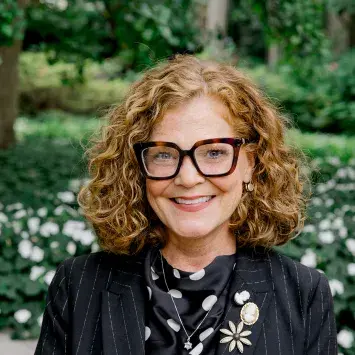 melanie turner looking at camera with black blazer and green background outside