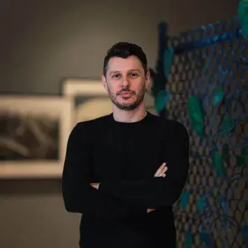 Headshot of Aaron Garvey in art gallery wearing a dark shirt, with art in the background