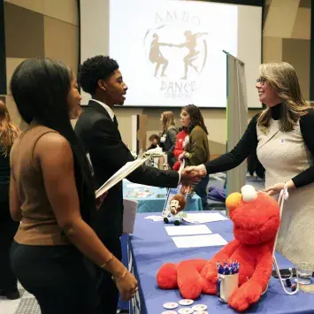 people shaking hands across table with elmo plush in foreground