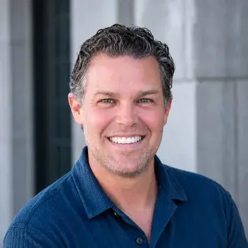 Headshot of Ryan Beeken wearing a dark blue button up shirt and smiling at the camera.