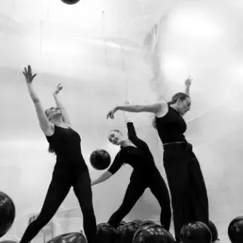 Black and white images of three dancers making various shapes with their bodies while dark balloons float around them.