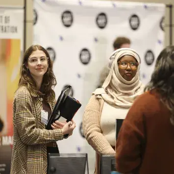 Two students at the Department of Arts Administration table talk with a visitor during a campus event.