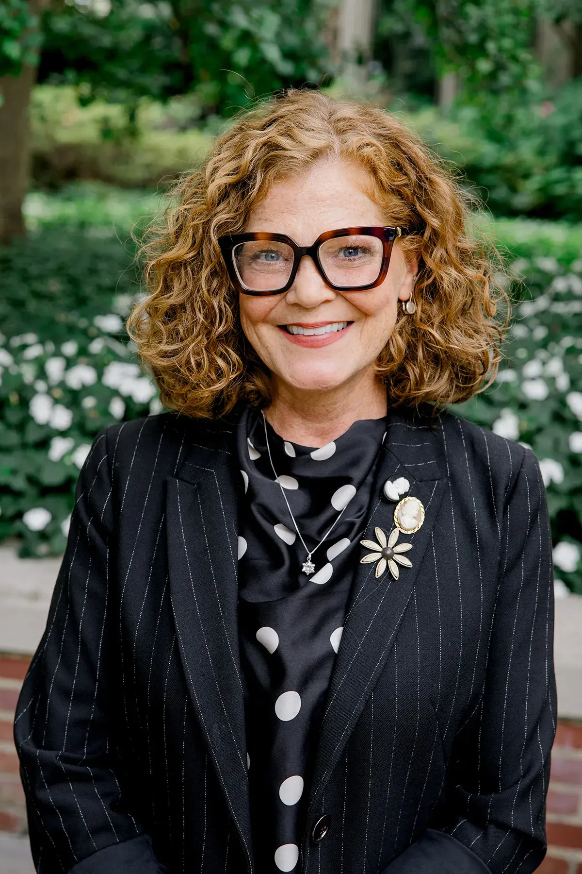 melanie turner looking at camera with black blazer and green background outside