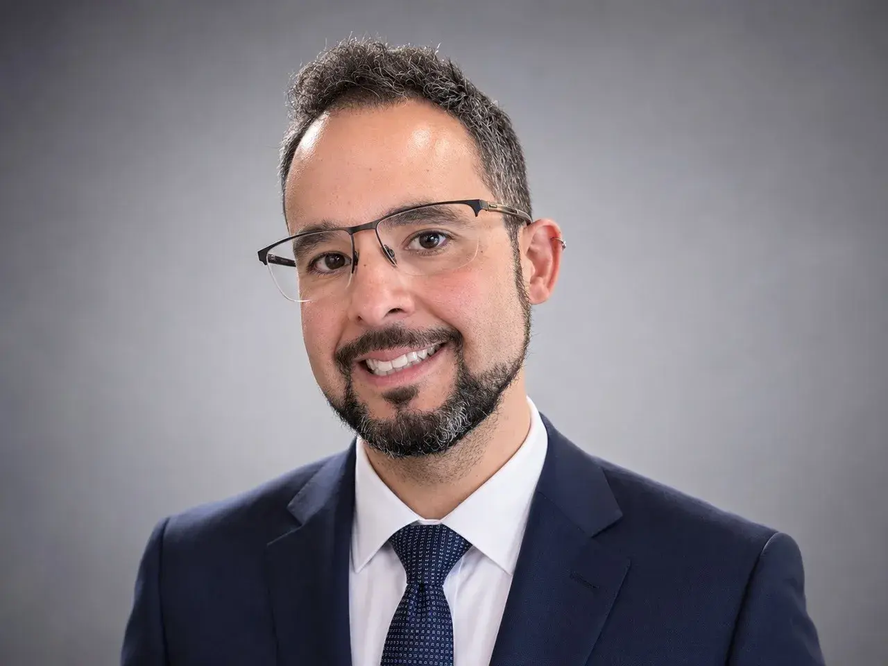 Michael Ibrahim wearing a dark blue suit and glasses smiling