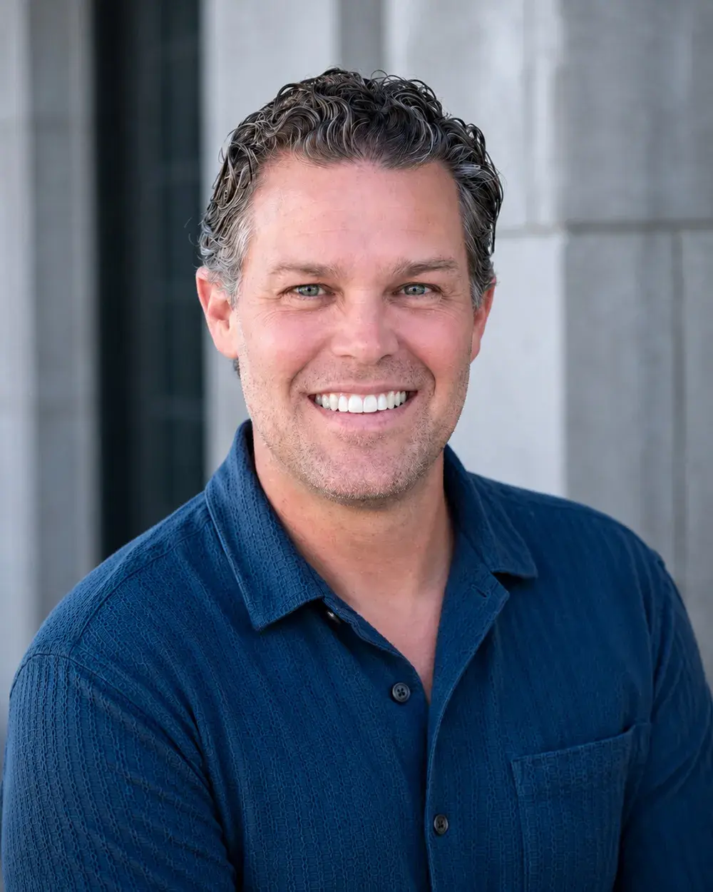 Headshot of Ryan Beeken wearing a dark blue button up shirt and smiling at the camera.